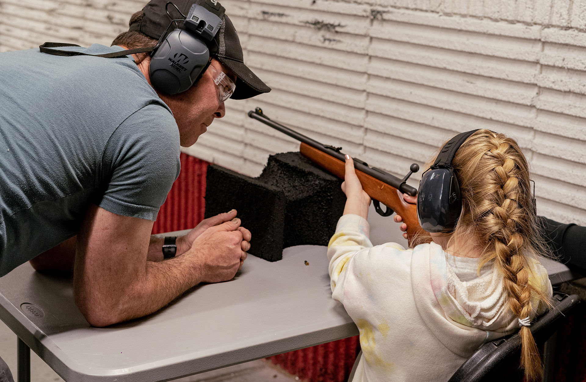Gun tutor watches young girl aim firearm